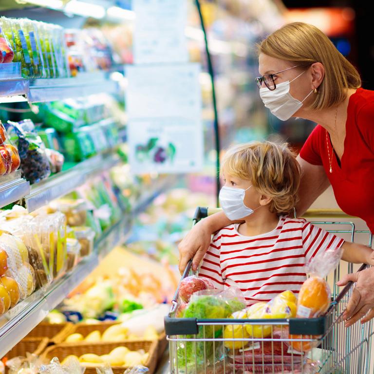 mother and child grocery shopping while wearing masks